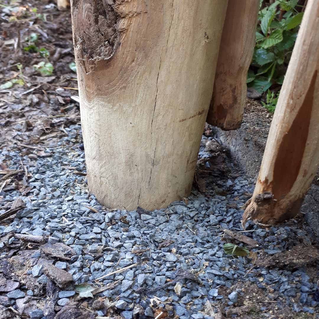 Detailansicht eines im Kiesbett eingebetteten Zaunpfahls aus Kastanienholz, Teil der Staketenzauninstallation